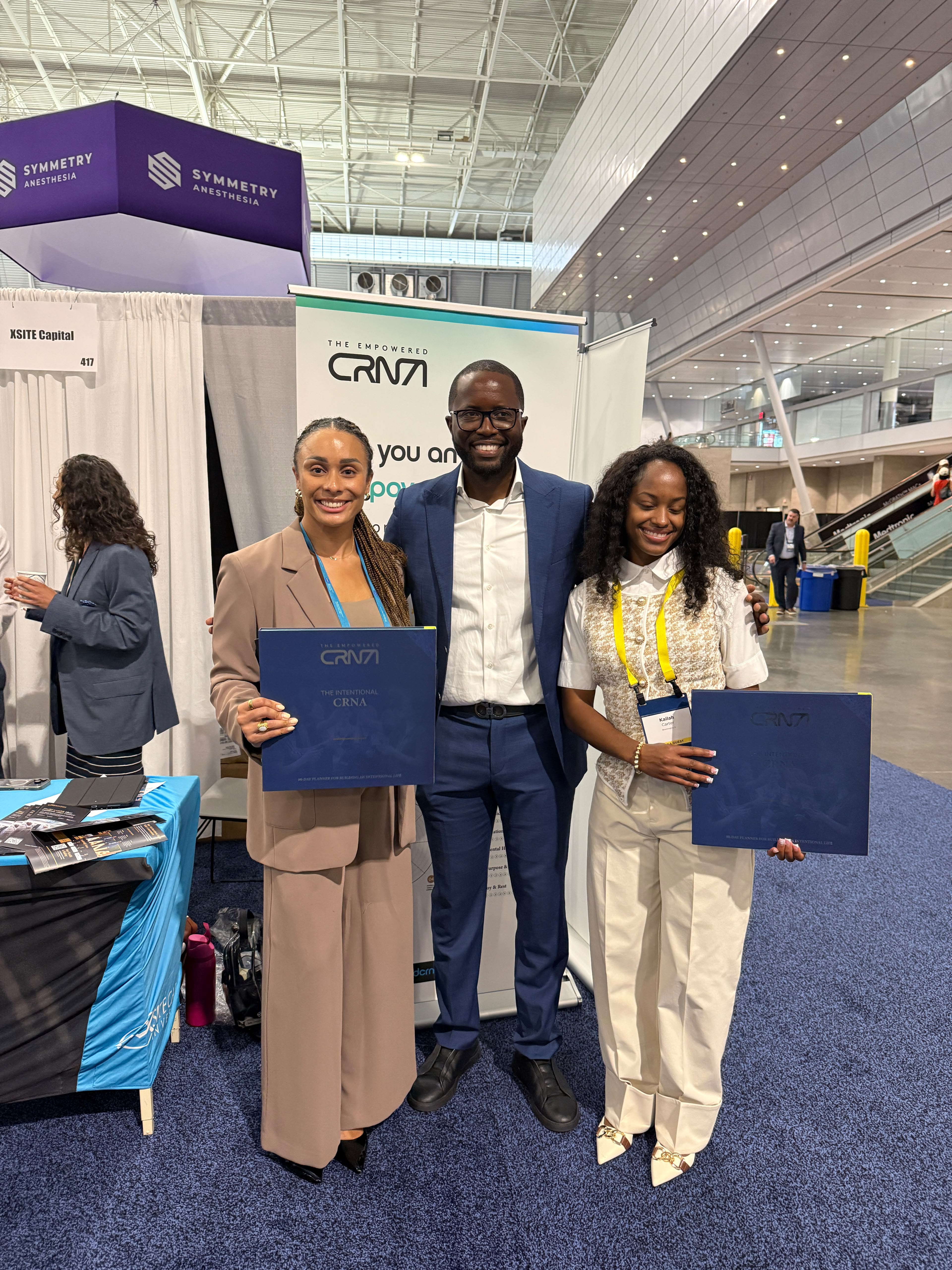 Leslie Awasom with CRNAs holding The Intentional CRNA journal at AANA 2026