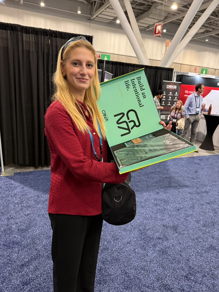 A CRNA at AANA 2026 smiling and holding an open copy of The Intentional CRNA, showing the "Build an Intentional life." inside cover