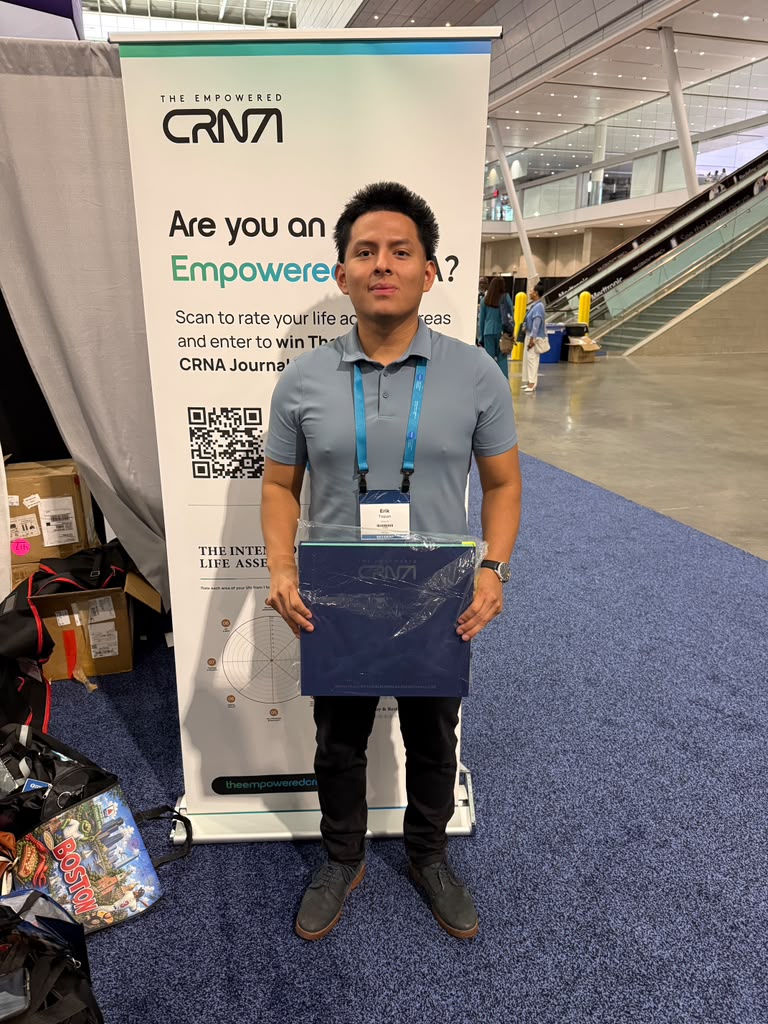 A CRNA holding a copy of The Intentional CRNA in front of the Empowered CRNA booth banner at AANA 2026